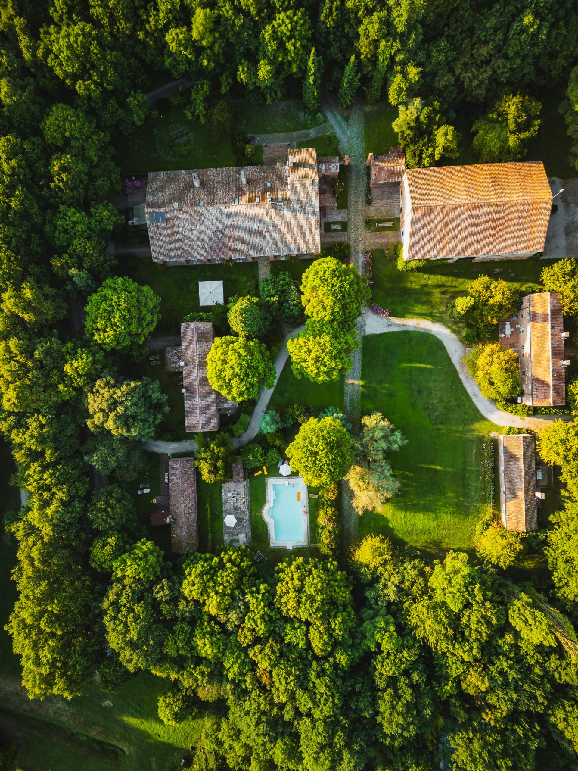 Stunning aerial view of a rustic villa surrounded by lush greenery in Italy's countryside.