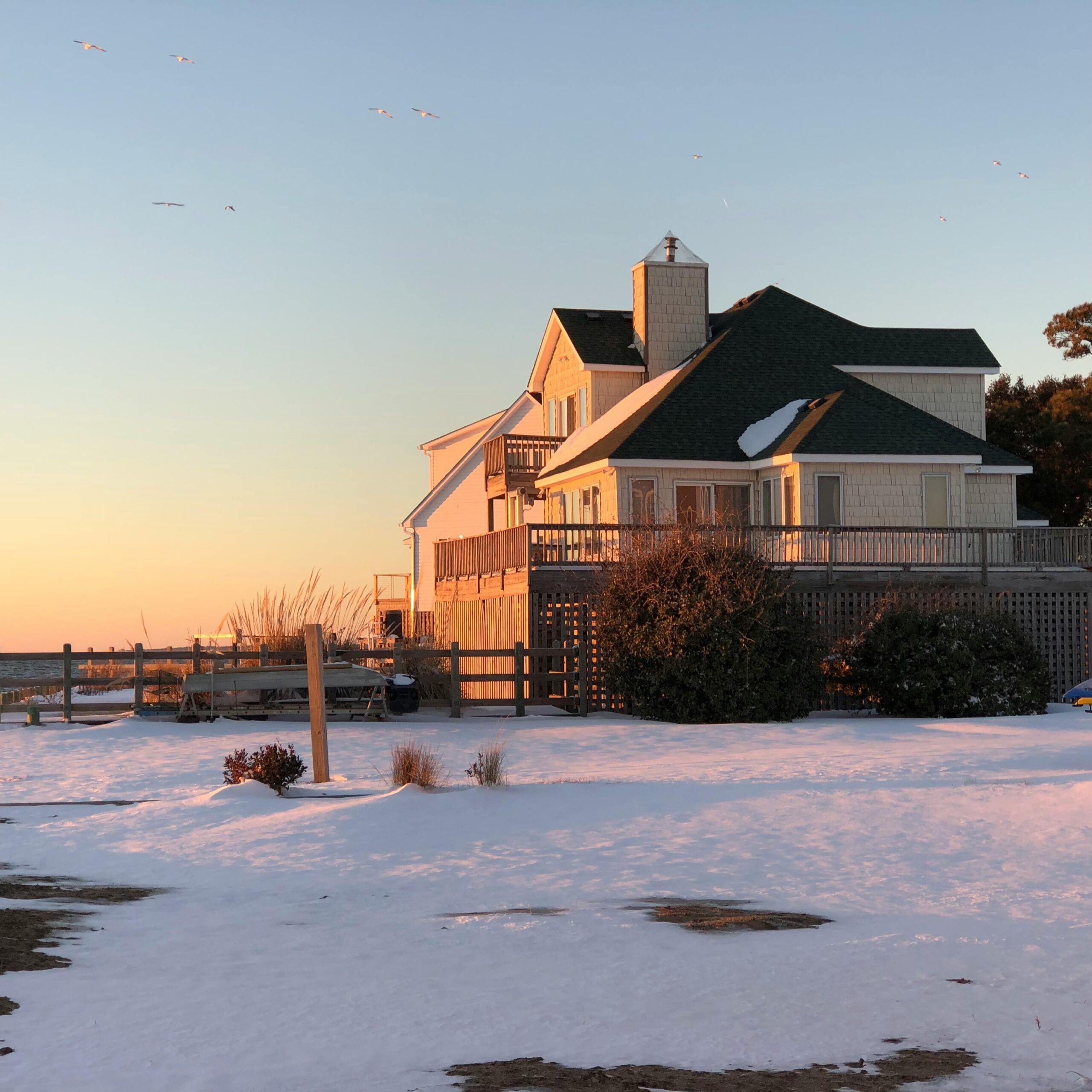 Charming beach house in Kill Devil Hills, NC, covered in snow during a serene sunset.